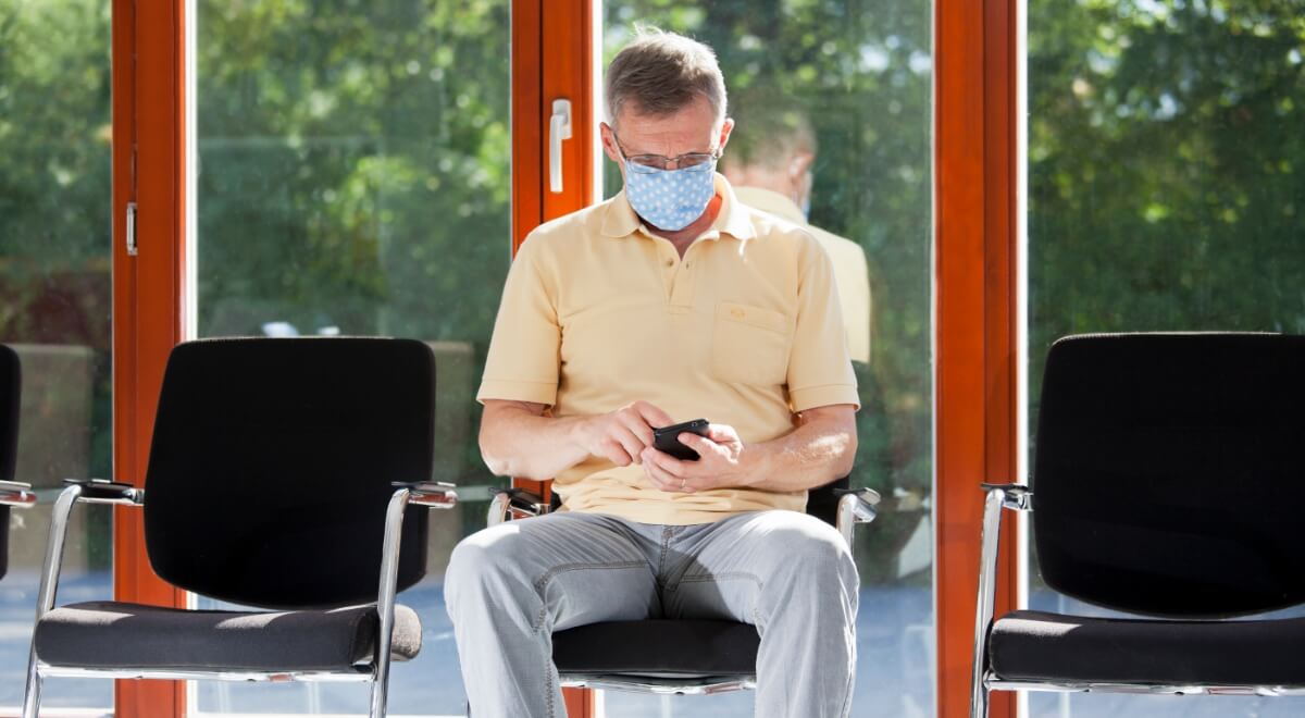 Man seated, wearing mask, using cell phone
