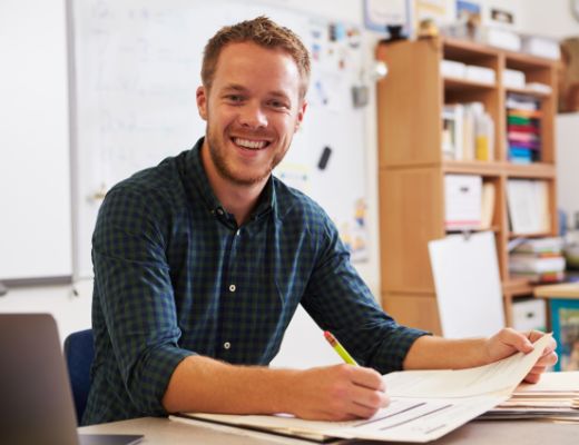 Smiling male teacher sitting at a desk grading papers