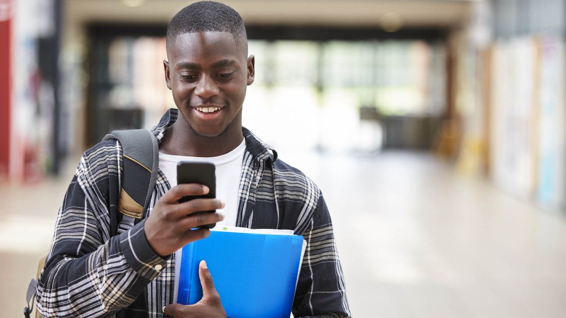 Student smiling holding a phone and folders